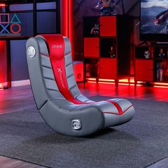 a grey and red gaming chair sitting on top of a carpeted floor in front of televisions