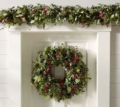 a wreath is hanging on the front door with greenery around it and red berries