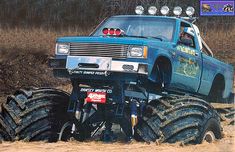 a blue truck with big tires driving in the mud