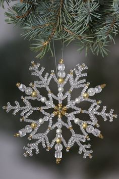 a snowflake ornament hanging from a pine tree with white and gold beads