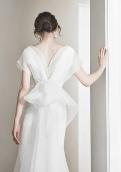 a woman in a white wedding dress is standing by a wall with her back to the camera