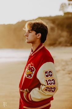 a young man standing on top of a beach next to the ocean wearing a red and white jacket