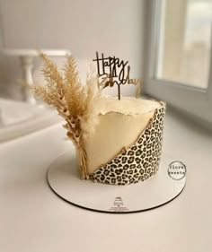 a leopard print cake with a happy birthday topper and some dry grass on it