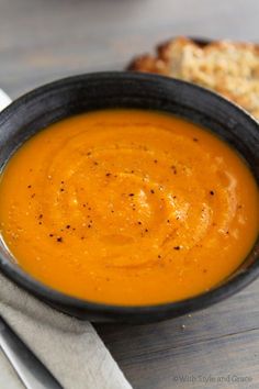 there is a bowl of soup on the table next to some slices of bread and silverware