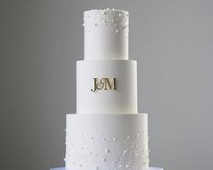 a three tiered wedding cake with white frosting and gold initials