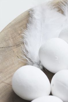 some white eggs are sitting on a wooden plate next to an open feather quill