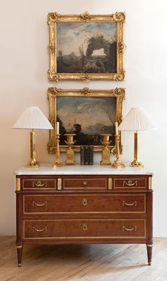 an antique dresser with two lamps and paintings on the wall