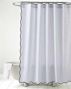 a white shower curtain with black scalloped edges on a bathroom floor next to a toilet