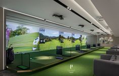 an indoor golf course with green carpeting and white ceiling lights, two gray couches and chairs in the foreground