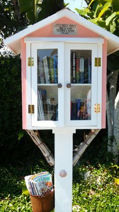 a white and pink book stand with books on it's shelves in the grass