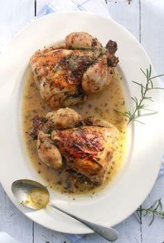 two chicken legs covered in gravy and garnished with herbs on a white plate