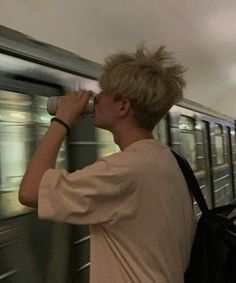 a young man drinking from a cup while standing in front of a subway train as it passes by