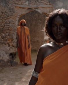 a woman in an orange dress is walking down the street with another person behind her