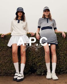 two young women in tennis outfits standing next to each other on top of a hedge