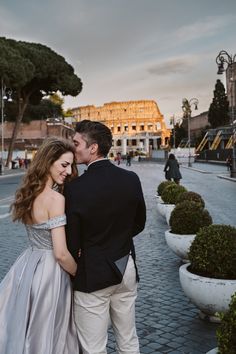 a man and woman standing next to each other in front of a building on a cobblestone street