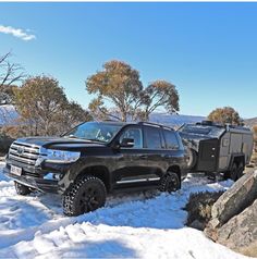 a black truck parked on top of snow covered ground next to a camper trailer