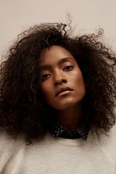 a woman with curly hair wearing a white sweater and black polka dot collared shirt