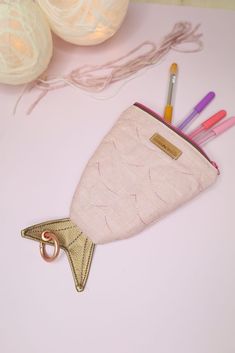 a pink pouch with pens and pencils in it sitting on a table next to yarn