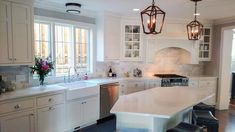 a kitchen with white cabinets and an island in the middle is lit by two hanging lights