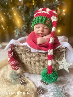 a newborn baby wearing a red and green hat in a basket next to a christmas tree