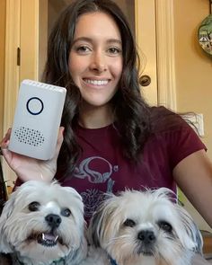 a woman holding two small white dogs in front of her and an electronic device on top of her