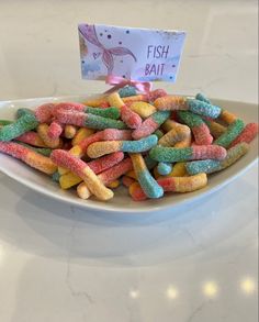 a white plate topped with lots of rainbow colored candy worms next to a sign that says fish ball