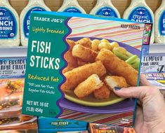 a person holding up a box of fish sticks in front of some other food items