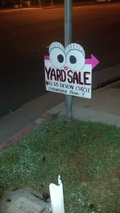 a yard sale sign on the corner of a street with grass and sidewalk lights in the background