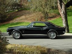 an old black car is parked on the side of the road in front of some trees