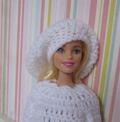 a doll wearing a white crocheted hat and dress with pink lips is next to a striped wall