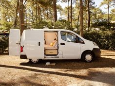 a small white van is parked in the woods with its door open and it's seat up