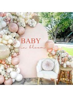 a baby shower backdrop with balloons and flowers on the wall, in front of a chair