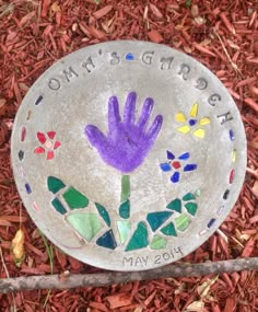 a stone with a purple hand painted on it sitting in the ground next to red mulch