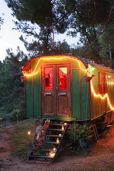 a green and yellow train car with christmas lights on it's side in the woods