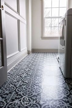 an empty kitchen with black and white flooring next to a refrigerator in the corner