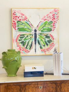 a green vase sitting on top of a wooden table next to a painting and books