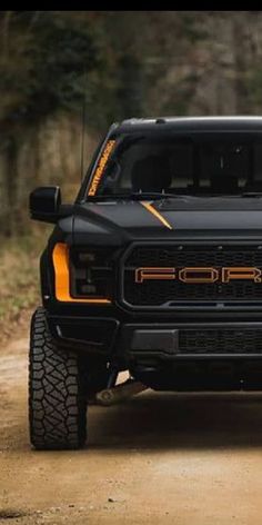 the front end of a black truck on a dirt road with trees in the background