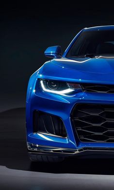 the front end of a blue chevrolet camaro in a dark room with its lights on