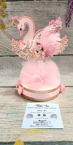 a pink hat with a swan on it and some feathers in the center, sitting on a wooden table