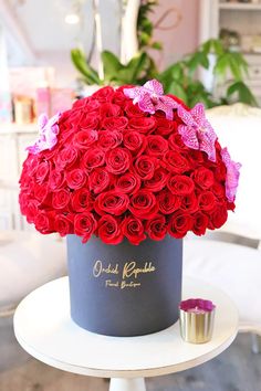 a large bouquet of red roses in a hat box on a table with a cup