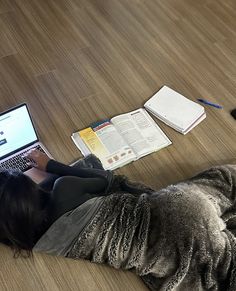 a woman is laying on the floor with her laptop and books in front of her