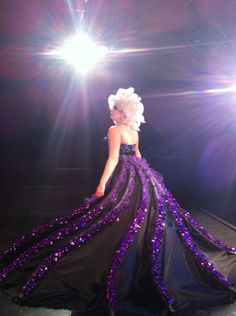 a woman in a purple and black dress is standing on stage with bright lights behind her