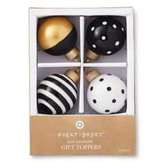 four black and white christmas ornaments in a gift box with gold accents on the top