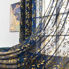 a blue and gold curtain with leaves on it in front of a painting hanging on the wall