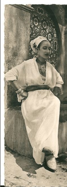 an old black and white photo of a woman sitting on a stone wall with her legs crossed