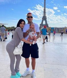 a man and woman holding a baby in front of the eiffel tower