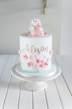 a white cake with pink flowers and a teddy bear on top that says algon