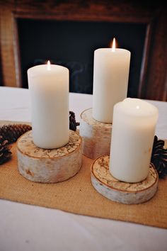 three white candles are sitting on wood slices