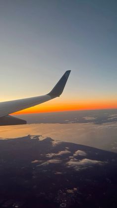 the wing of an airplane as it flies through the sky above clouds at sunset or dawn