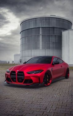 a red sports car is parked in front of a large silo on a cloudy day